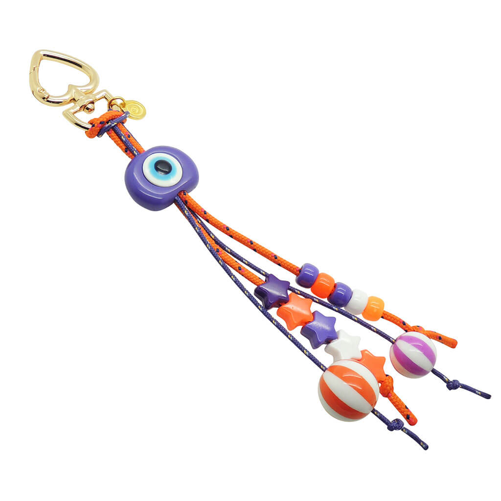 Dana Levy Evil Eye Circus Bag Charm with a purple evil eye amulet and orange and purple cords and charms.  